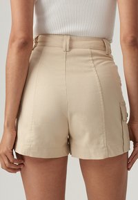 Beige högmidjade shorts med en smal passform, som har sidofickor, en mjuk yta och synliga sömmar längs fållen.