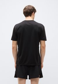 Svart sportt-shirt med korta ärmar, slät tyg och subtila sidospjälor. Bakifrån syns en enkel design och en avslappnad passform.