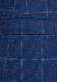 Niebieska tkanina w kratę o teksturowanym splocie. Posiada czerwone i kremowe linie w kratę. Zawiera naszywaną kieszeń na dopasowanym elemencie.