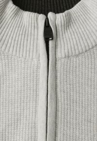 Svetr na zip v světle šedé barvě s ribkovanou texturní látkou. Obsahuje vysoký límec a černý zip. Materiál vypadá měkký a texturovaný.