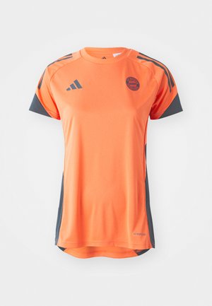 T-shirt de sport orange avec des accents gris, à manches courtes, col rond et logo du Bayern de Munich sur la poitrine. Fabriqué en matériau léger.