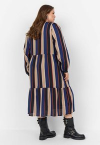 Robe rayée à manches longues, présentant des rayures marine, beige et rouille. Ourlet évasé, taille froncée, portée avec des bottines noires.