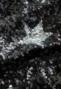 Tissu noir densément couvert de sequins noirs et argentés brillants créant une surface scintillante et texturée avec des reflets de lumière.