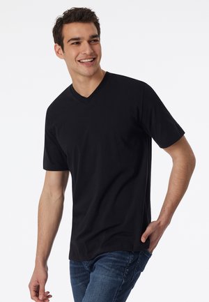 Zwarte v-hals t-shirt van katoen, met korte mouwen en een relaxte pasvorm, gecombineerd met blauwe denim jeans. Eenvoudig ontwerp, zonder patronen.