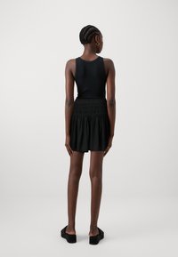 Μαύρο αμάνικο τοπ συνδυασμένο με μαύρη, φλοωτή φούστα με ραμμένη μέση. Το μοντέλο φοράει χοντρές μαύρες παπούτσια, δείχνοντας μια απλή σιλουέτα.