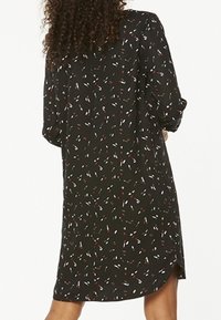 Czarna sukienka z rozproszonym wzorem białych i czerwonych kształtów. Długie rękawy, boczne rozcięcia i luźny krój. Lekka, gładka tkanina.