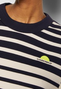 Pruhovaný top s krátkým rukávem v námořnické modré a krémové barvě. Má žebrovaný límec a malý zelený logo detail s textem "CLAUDIE PIERLOT".
