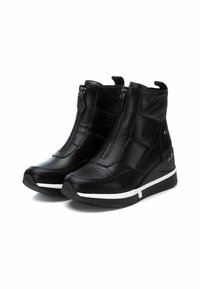 Botines negros de cuero texturizado, con cremalleras en los laterales, un acento de entresuela blanca y un tacón en cuña para mayor elevación.