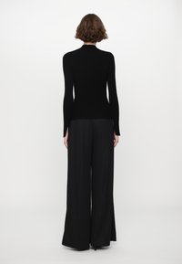 Black ribbed turtleneck sweater paired with loose-fitting black trousers. The outfit features a fitted design and long sleeves with side slits.