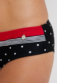 Schwarze Bikinihose mit weißen Punkten und roten Streifen. Auf der Seite befindet sich ein kleines silbernes Logo-Detail. Glattes, dehnbares Material.