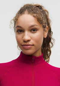 Piemērots, ribots, ar rāvējslēdzēju augšpusē topiņš košā magentā. Ar augstu apkakli un garām piedurknēm. Gluda tekstūra, pielāgota sega aktīvai lietošanai.