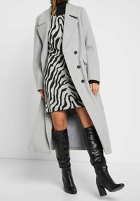 Szary wełniany płaszcz o strukturalnym kroju, czarna sukienka w zebrę oraz czarne skórzane kozaki za kolano na obcasie typu bloczek.