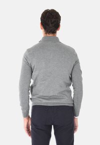 Maglione grigio lavorato a maglia con colletto alto, caratterizzato da maniche lunghe e un design aderente, abbinato a pantaloni scuri. Texture del tessuto liscia.