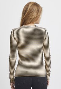Cămașă cu mânecă lungă, cu o textură ribbed și dungi negre pe un fundal bej. Design minimalist, cu guler rotund.
