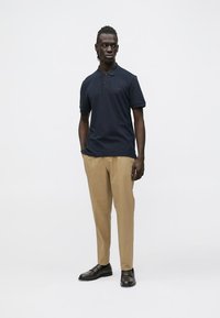 Navy polo shirt with a collar and short sleeves, paired with beige trousers, complemented by black shoes. Simple and tailored fit.