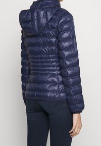 Chaqueta acolchada azul marino con capucha, que presenta un diseño acolchado y una textura brillante, mostrada desde la parte trasera.