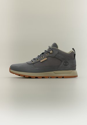 Γκρι sneaker μέσης ανόδου Timberland με μπεζ σόλα, δέσιμο με κορδόνια μπροστά και λογότυπο στο πλάι, εμφανίζεται σε ουδέτερο φόντο.