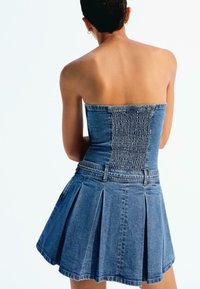 Jeans obleka s prilegajočim, ruffled zgornjim delom in nabranim krilom. Ima brez naramnic in svetlo modro barvo.