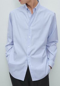 Camicia abbottonata di un blu chiaro con righe verticali bianche, colletto classico, maniche lunghe e vestibilità rilassata. Tessuto leggermente texturizzato.