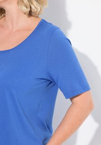 Modrý top s krátkým rukávem a kulatým výstřihem, vyrobený z měkké tkaniny. Disponuje jednoduchým designem, hladkým texturem a minimem švů.
