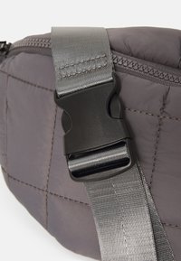 Borsa a tracolla grigia imbottita con cinturino testurizzato e chiusura in plastica nera. Il tessuto presenta dettagli di cuciture orizzontali.