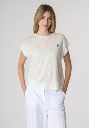 Top corto bianco leggero e semitrasparente con maniche corte e scollo a girocollo, dotato di un piccolo logo sul lato sinistro del petto. Abbinato a pantaloni bianchi larghi.