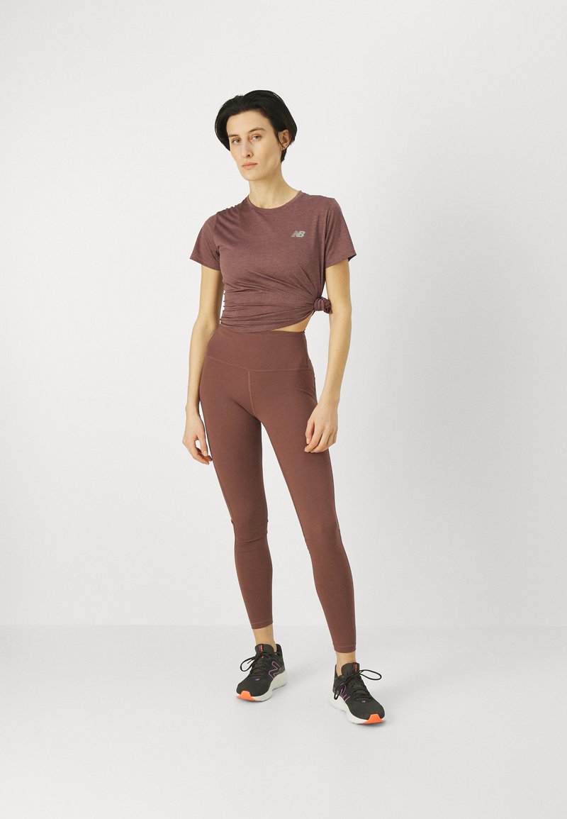 Tenue de sport avec un haut bordeaux à manches courtes et torsadé, accompagné de leggings taille haute assortis. Baskets noires avec des accents orange.