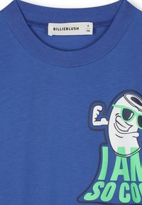 Blauwe katoenen t-shirt met een ronde hals. Heeft een speelse graphic van een lachend figuur met een zonnebril en de tekst "IK BEN ZO COOL" in het groen.