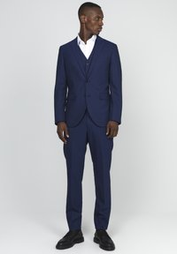Temno modra trodelna obleka s slim fit krojem, z zarezani reverji in dvema gumboma. Kombinirana z belo srajco in črnimi elegantnimi čevlji.