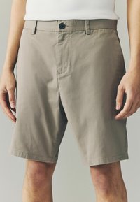Khaki šortsevi napravljeni od laganog materijala, sa kopčanjem na dugme, prednjim džepovima i glatkom teksturom, ravnog kroja do koljena.