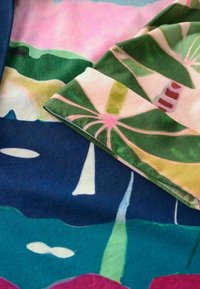 Tissu à motifs colorés présentant des designs abstraits dans des nuances de vert, rose, bleu et violet, avec une trame légère et texturée.