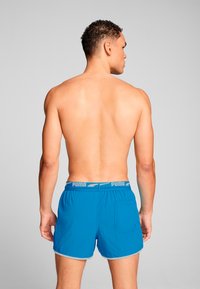 Bañador azul con cinturilla elástica que presenta un acento gris. Fabricado con una tela ligera, tiene un bolsillo trasero y un corte relajado.