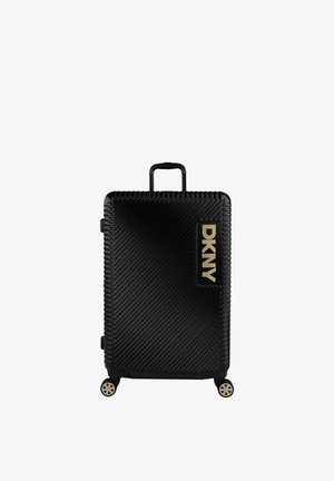 Maleta rígida negra con ranuras diagonales, logo dorado de DKNY, asa retráctil, cuatro ruedas y superficie texturizada para un mejor agarre.