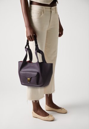 Purple leather handbag with a front pocket and gold hardware; worn with light-colored, frayed hem trousers and beige flats.