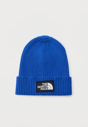 Blue knitted beanie with ribbed texture, featuring a black patch with "The North Face" logo on the front. Soft material, form-fitting design.
