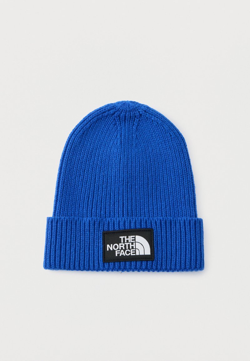 Gorro de punto azul con textura acanalada, que presenta un parche negro con el logotipo de "The North Face" en el frontal. Material suave, diseño ajustado.