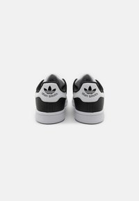 Zapatillas en blanco y negro con parte superior de cuero suave, puntera redonda y talón acolchado. Presentan un logotipo en la etiqueta del talón y una suela de goma texturizada.