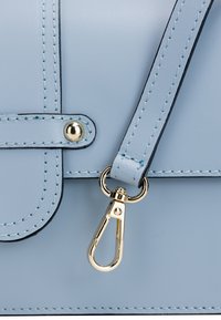 Lyseblå lædertaske med guldfarvet hardware, der har en lås og kontrasterende syninger. Glat overflade og rektangulær form.