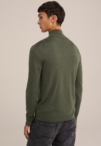 Suéter de punto verde con cuello alto, diseño ajustado y mangas largas. Textura con patrón y dobladillo acanalado. Combinado con jeans grises.