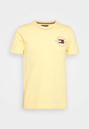 Jasnożółta koszulka z krótkim rękawem z małym logo Tommy Hilfiger i napisem na górnej lewej części klatki piersiowej.