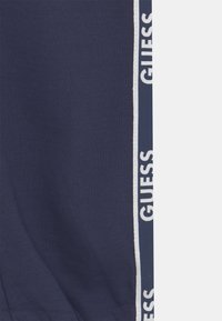Navyblauwe katoenen joggers met een witte "GUESS" logo-streep aan de zijkant. Soepele textuur met een ontspannen pasvorm.