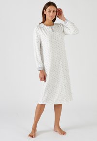 Lange witte nachtjapon met een klein bloemenpatroon, lange mouwen, grijze manchetten en een knoopsluiting bij de hals. Zachte stof, losse pasvorm, lengte tot halverwege de kuiten.