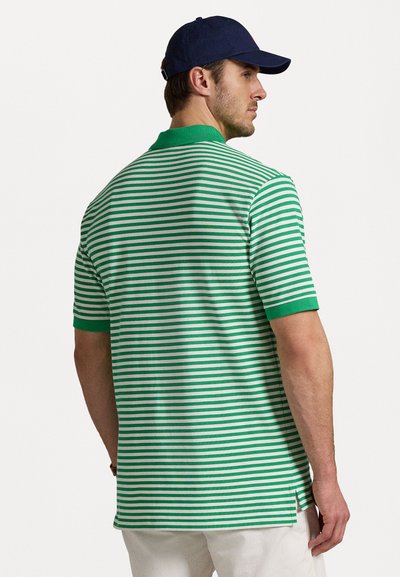 Tricou polo cu dungi verzi și albe, cu mâneci scurte, guler ribbed și fante laterale. Purtați cu o șapcă bleumarin. Design ajustat.