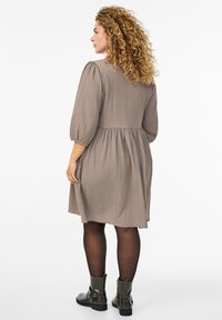 Brun klänning med struktur, puffiga ärmar, markerad midja och utsvängd kjol. Bärs med svarta ankle boots. Bakifrån.