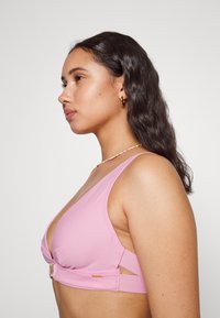 Top de natação rosa com decote profundo, apresentando recortes laterais e um fecho em tom dourado. Feito de um tecido suave com uma textura macia.