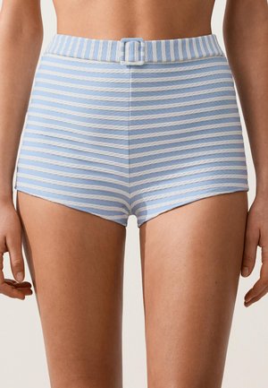 Frau trägt hoch taillierte blaue und weiße horizontal gestreifte Shorts mit Stoffgürtel und Schnalle an der Taille.