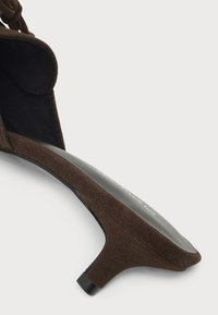 Καφέ σουέντ πέδιλο με χαμηλό μαύρο τακούνι kitten heel και λεπτό λουράκι σε λευκό φόντο.