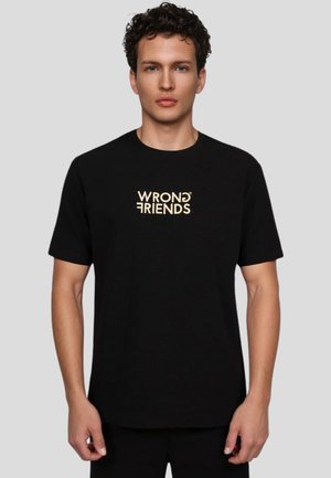 Sort T-shirt med korte ærmer, prydet med gyldent broderet tekst "WRONG FRIENDS" centreret på forsiden. Simpelt design, bomuldsstof.