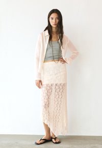 Lichtroze kant rok met een asymmetrische zoom, gecombineerd met een grijze tanktop en een doorzichtige, lichtroze overhemdd. Zwarte flip-flops.
