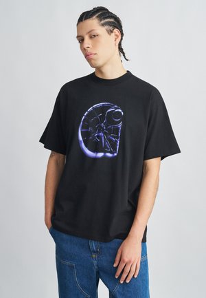 Camiseta negra de algodón con un gran gráfico circular con un diseño neon en azul y blanco, combinada con jeans de mezclilla azul. Corte casual.